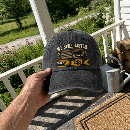 Handheld black vintage washed cap with printed radio design and “We Still Listen To The Whole Story” slogan