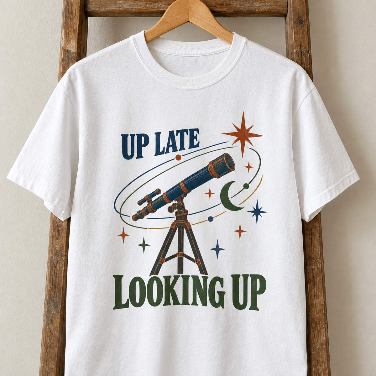 White vintage t-shirt hanging with printed Up Late Looking Up telescope design and stars