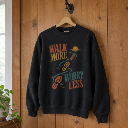 Black vintage sweatshirt with printed “Walk More. Worry Less” design, hanging against wood paneling