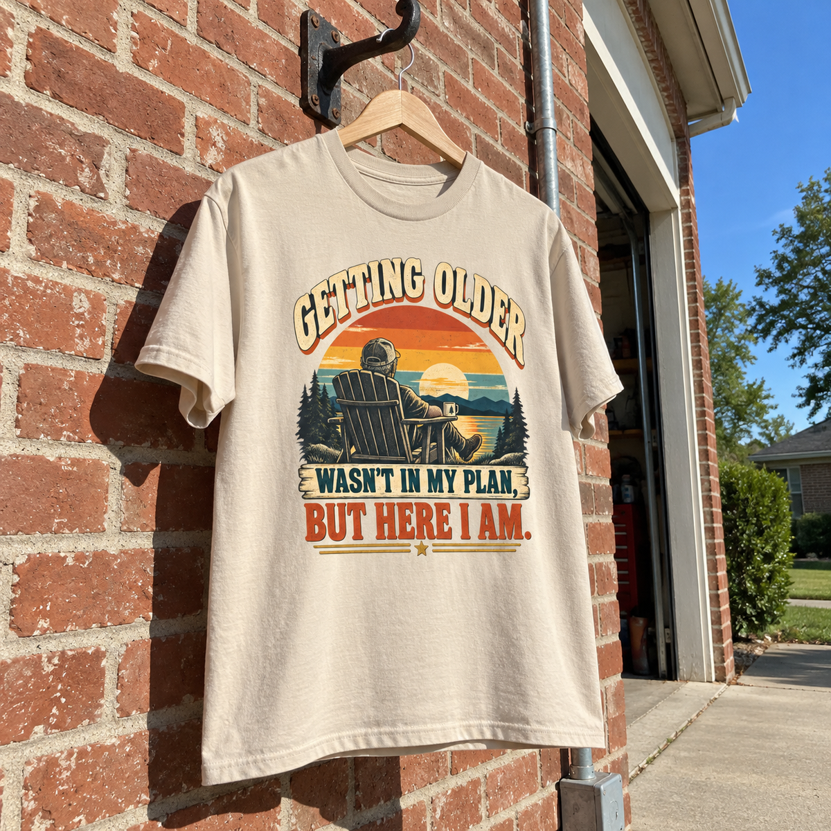 Cream vintage t-shirt hanging against brick wall with printed sunset and Getting Older slogan