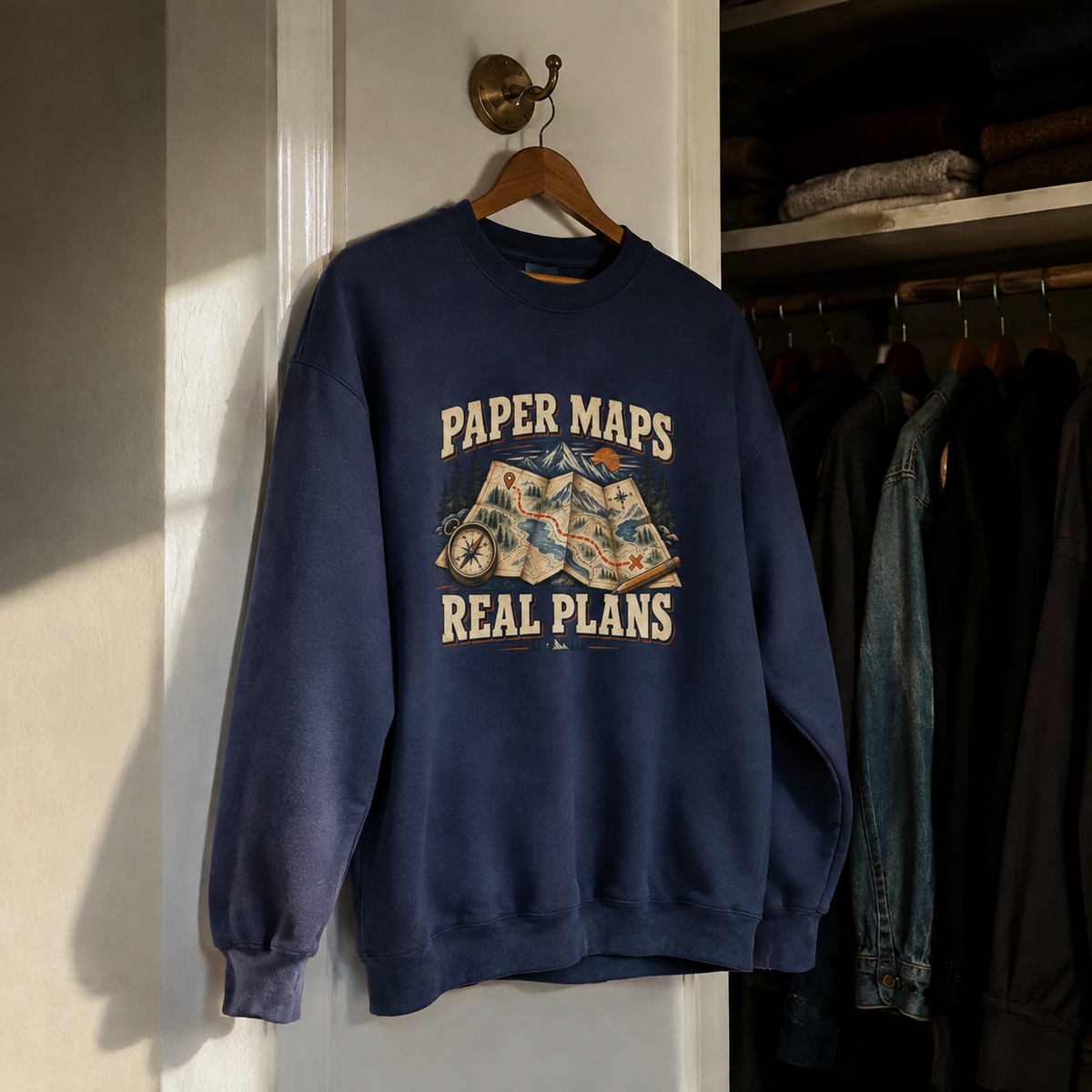 Navy vintage sweatshirt with printed Paper Maps Real Plans graphic hanging on wooden hanger