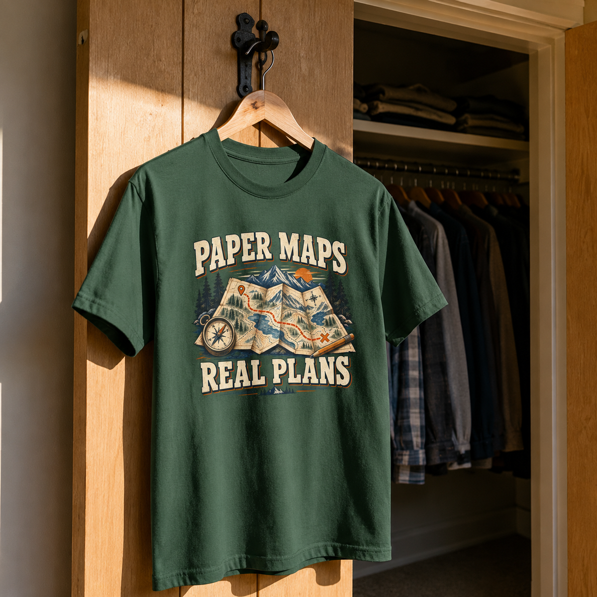 Green vintage t-shirt hanging with printed Paper Maps. Real Plans mountain map design.