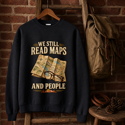 Black vintage sweatshirt with printed “We Still Read Maps And People” design hanging on a wooden hanger.