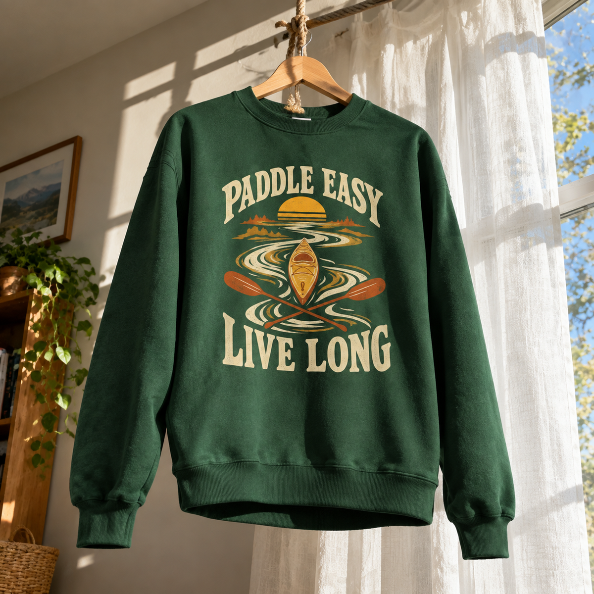 Green vintage sweatshirt with printed Paddle Easy Live Long kayaking design, hanging indoors