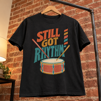 Black vintage t-shirt hanging on wooden hanger, printed with Still Got Rhythm and drum design.