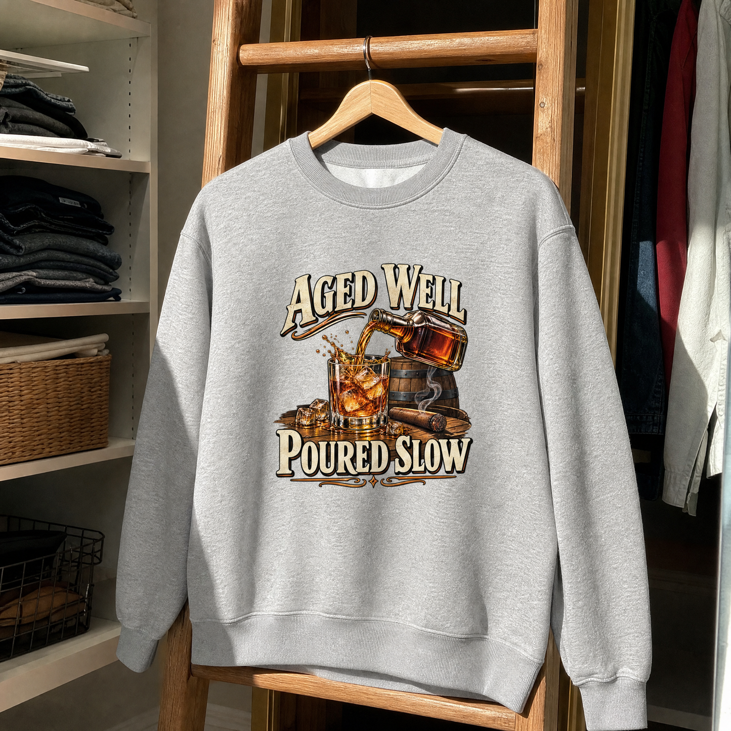 Gray vintage sweatshirt hanging with printed “Aged Well. Poured Slow” whiskey design.