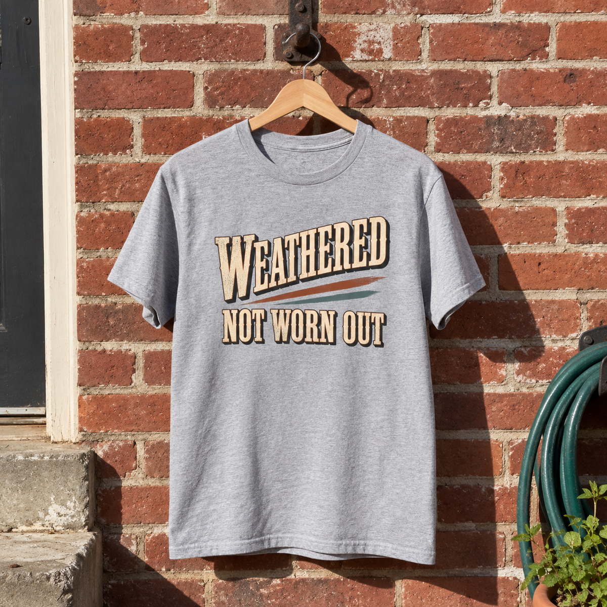 Gray vintage t-shirt with Weathered Not Worn Out print hanging against brick wall