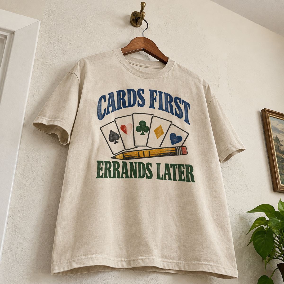Cream vintage t-shirt hanging, printed with Cards First. Errands Later and playing card graphics