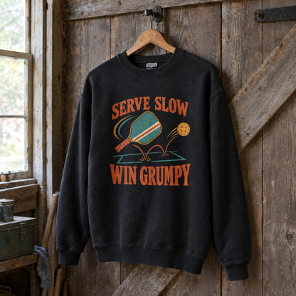 Black vintage sweatshirt hanging on a wooden wall with printed Serve Slow Win Grumpy design