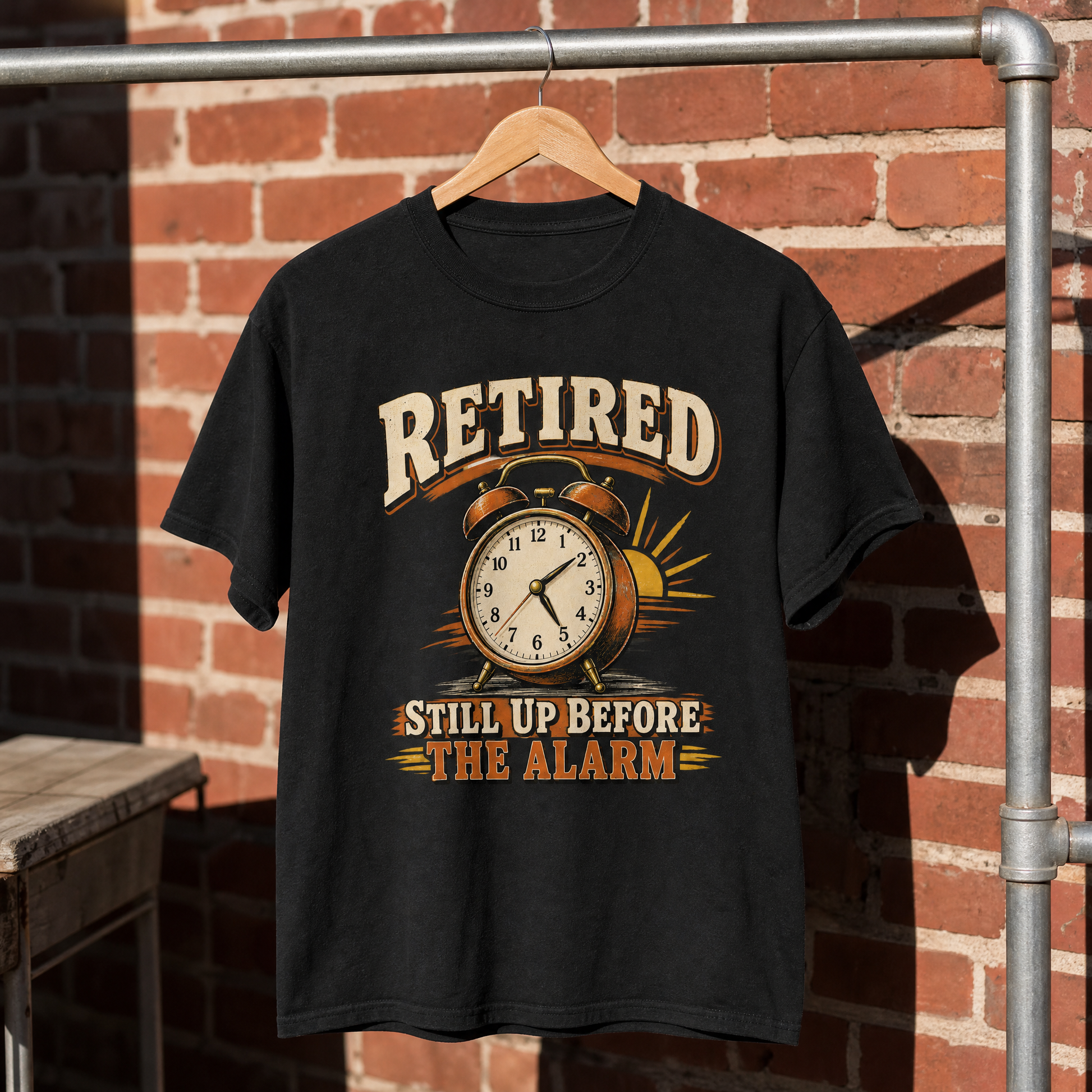 Black vintage t-shirt with printed “Retired Still Up Before The Alarm” design, hanging against brick wall