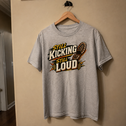 Gray vintage t-shirt hanging with printed Still Kicking Still Loud design