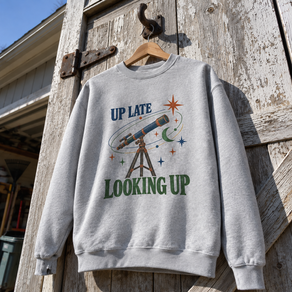 Gray vintage sweatshirt with Up Late Looking Up printed telescope design, hanging outdoors on wooden door