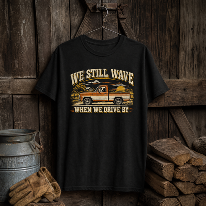 Black vintage t-shirt hanging with printed “WE STILL WAVE WHEN WE DRIVE BY” truck design.