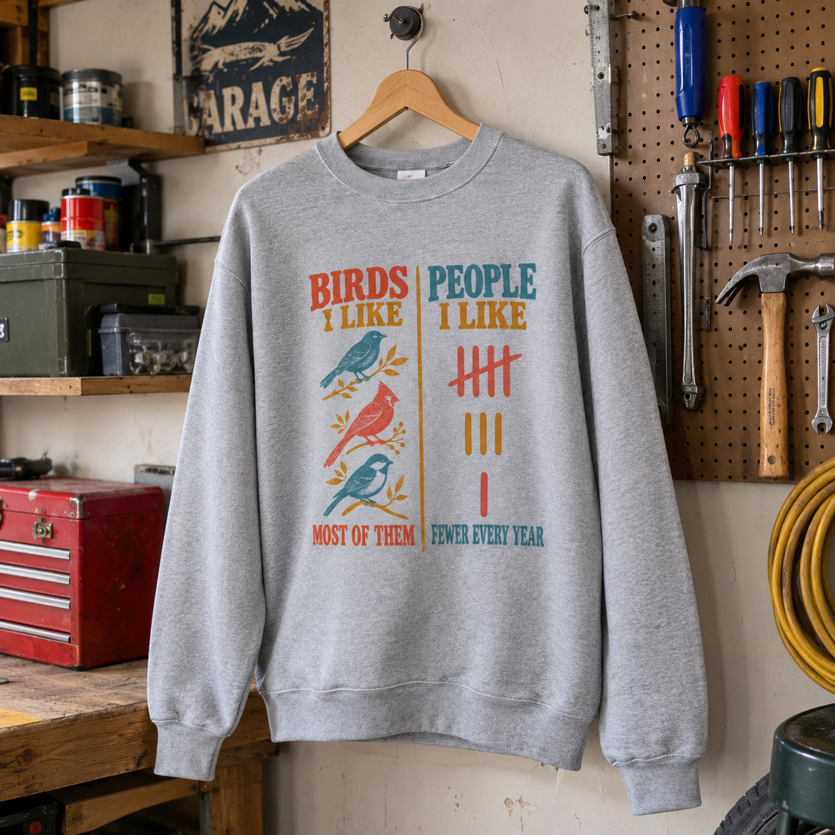 Gray vintage sweatshirt with printed Birds Like Most Of Them slogan hanging in a garage workshop