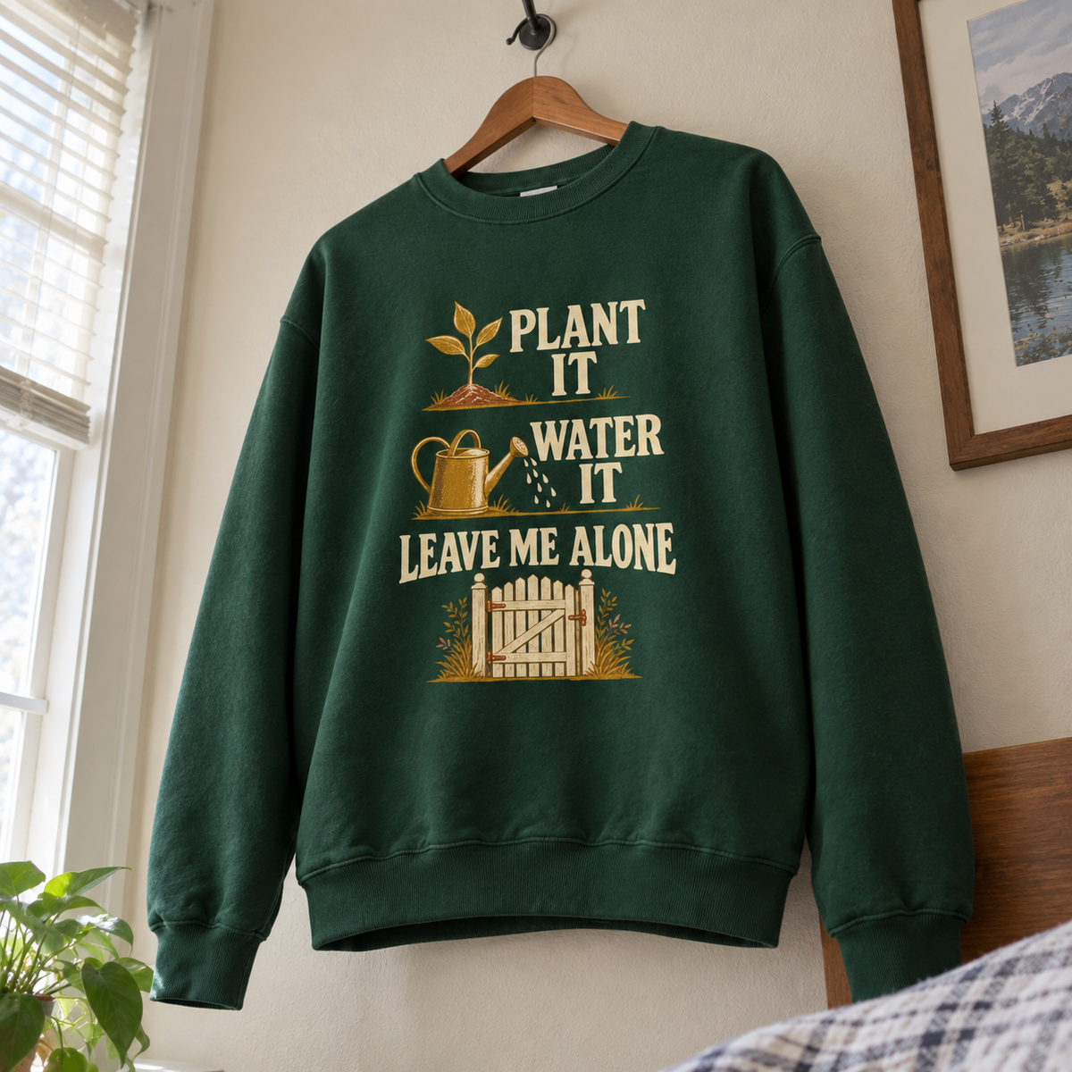 Green vintage sweatshirt hanging with printed plant, watering can, and “Leave Me Alone” design