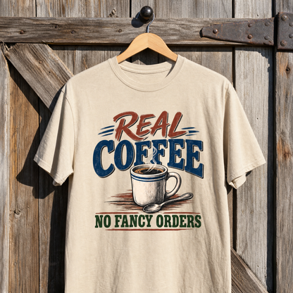 Vintage t-shirt hanging on wood, cream with printed “Real Coffee. No Fancy Orders” coffee graphic