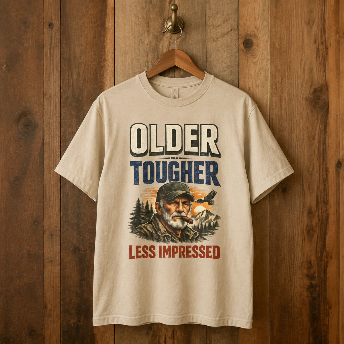 Cream vintage t-shirt hangs on wooden wall with Older Tougher Less Impressed printed design