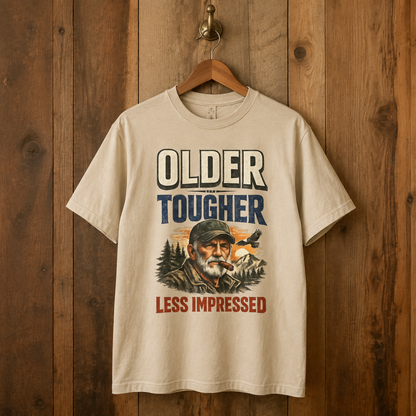 Cream vintage t-shirt hangs on wooden wall with Older Tougher Less Impressed printed design