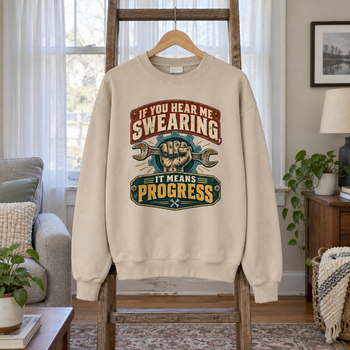 Cream vintage sweatshirt hanging on wooden ladder with printed swearing slogan and wrench design