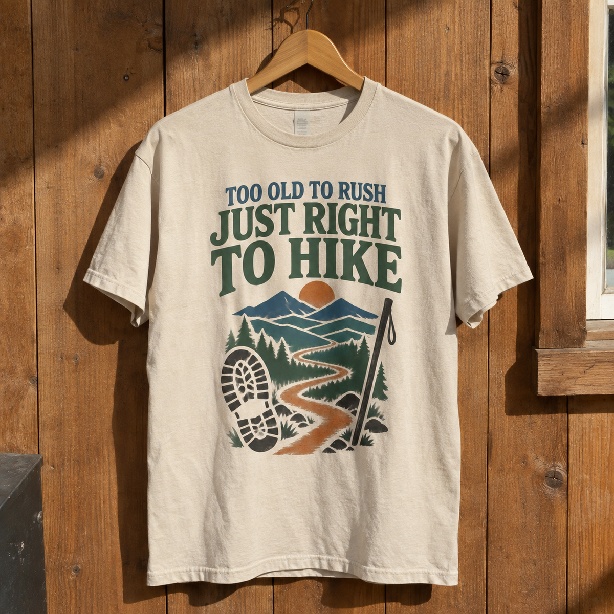 Cream vintage t-shirt hanging on wall, printed hiking scene and slogan Too Old To Rush.