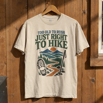 Cream vintage t-shirt hanging on wall, printed hiking scene and slogan Too Old To Rush.