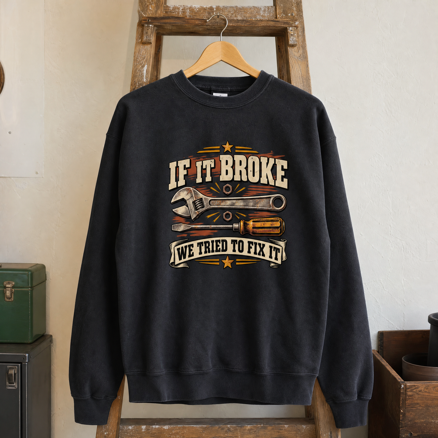 Black vintage sweatshirt hanging with printed “If It Broke We Tried To Fix It” slogan and tools