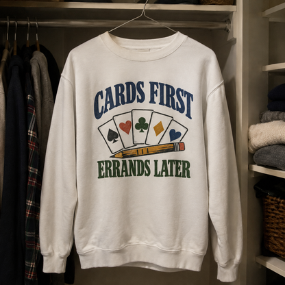 White vintage sweatshirt hanging with printed Cards First. Errands Later slogan and playing cards.