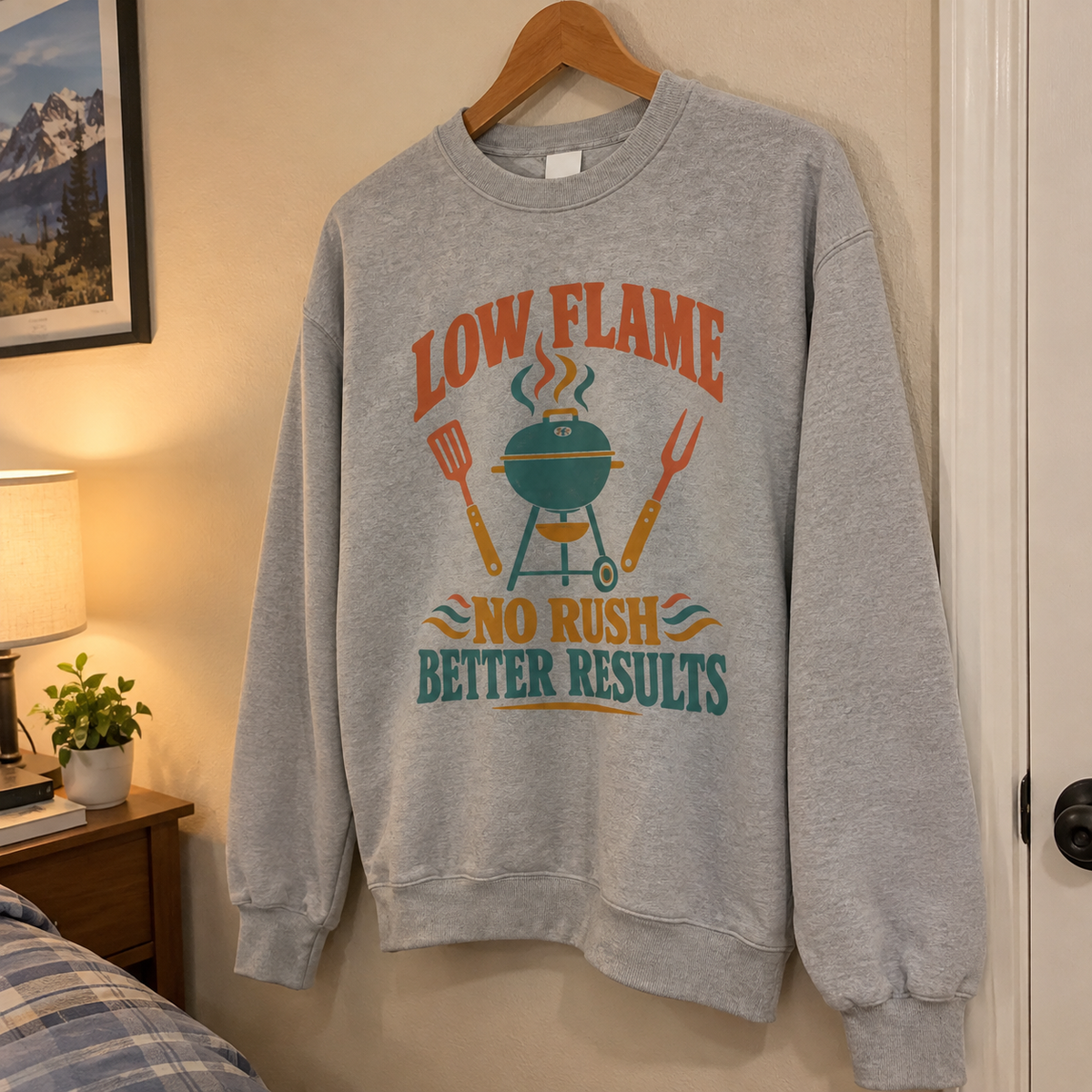 Gray vintage sweatshirt hanging with printed “Low Flame. No Rush Better Results” barbecue design.