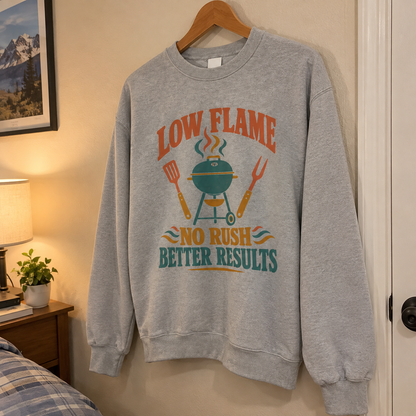Gray vintage sweatshirt hanging with printed “Low Flame. No Rush Better Results” barbecue design.