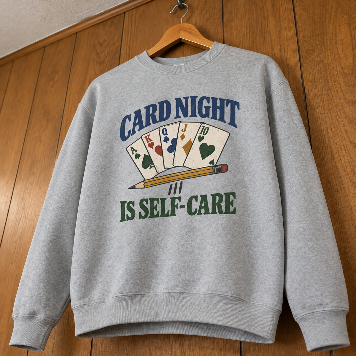 Gray vintage sweatshirt hanging with printed Card Night Is Self-Care design