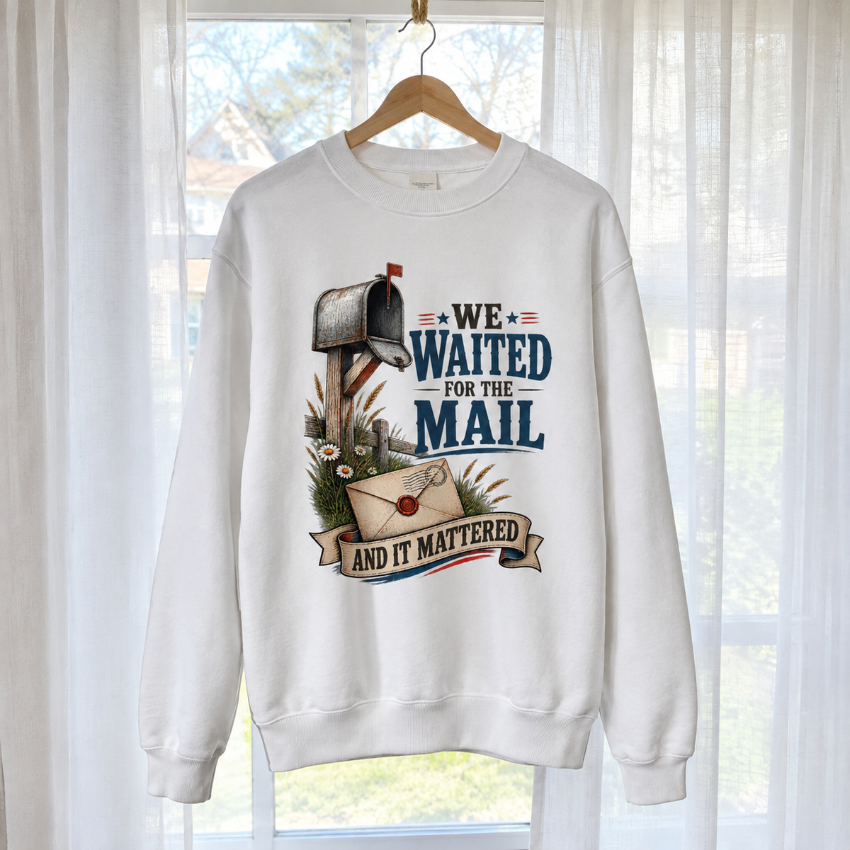 White vintage sweatshirt with printed mailbox and “We Waited For The Mail” slogan, hanging by window