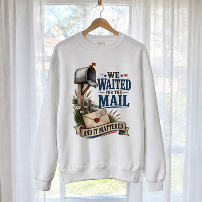 White vintage sweatshirt with printed mailbox and “We Waited For The Mail” slogan, hanging by window