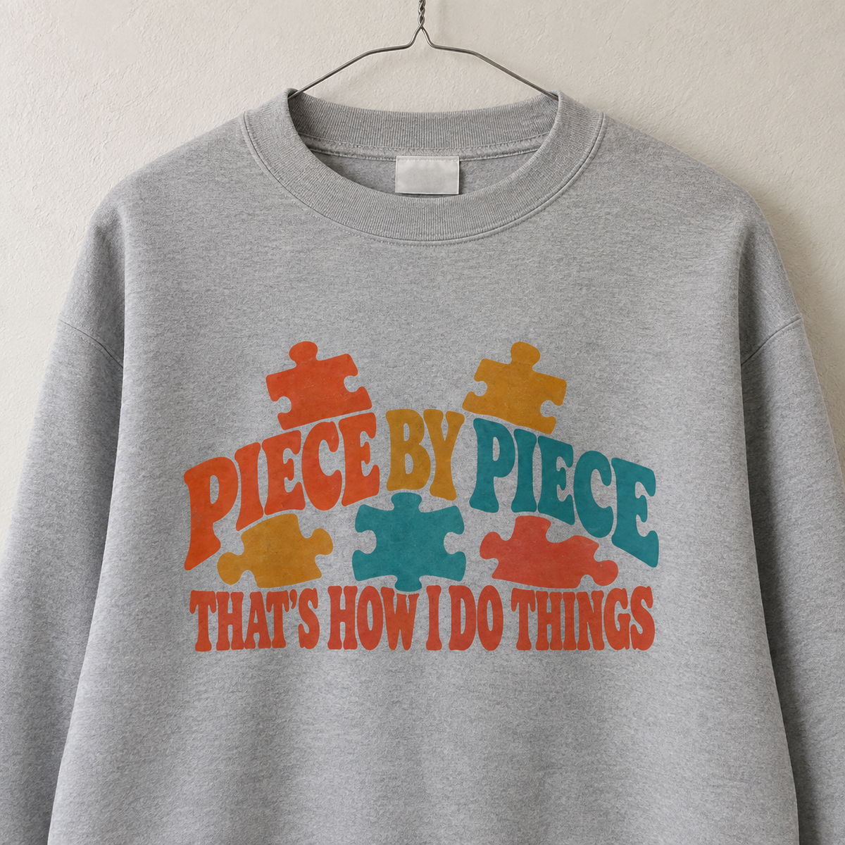Gray vintage sweatshirt hanging, printed puzzle pieces with Piece By Piece slogan
