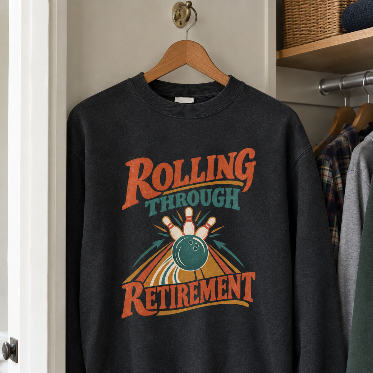 Black vintage sweatshirt hanging, printed "Rolling Through Retirement" bowling design in orange and teal.