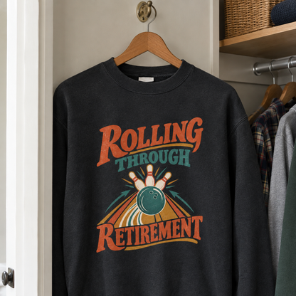Black vintage sweatshirt hanging, printed "Rolling Through Retirement" bowling design in orange and teal.