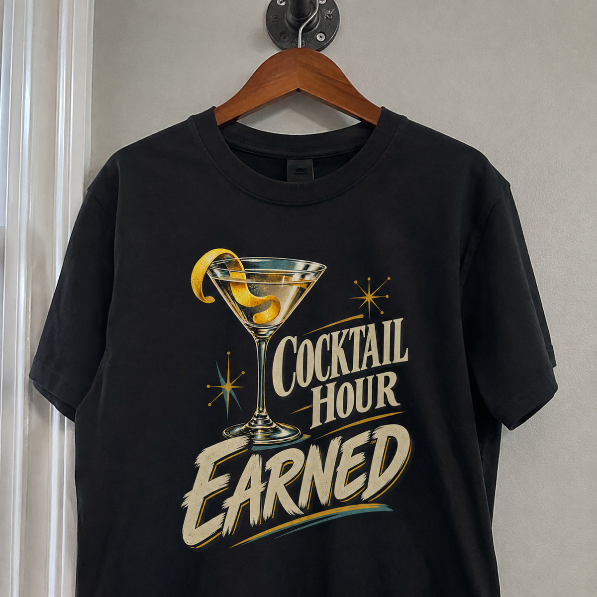Black vintage t-shirt hanging on a wooden hanger with printed Cocktail Hour Earned cocktail graphic