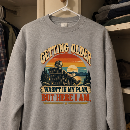 Gray vintage sweatshirt hanging, printed with “Getting Older Wasn’t In My Plan, But Here I Am”