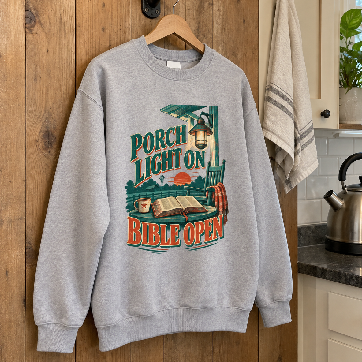 Gray vintage sweatshirt hanging on wooden door with printed Porch Light On Bible Open design