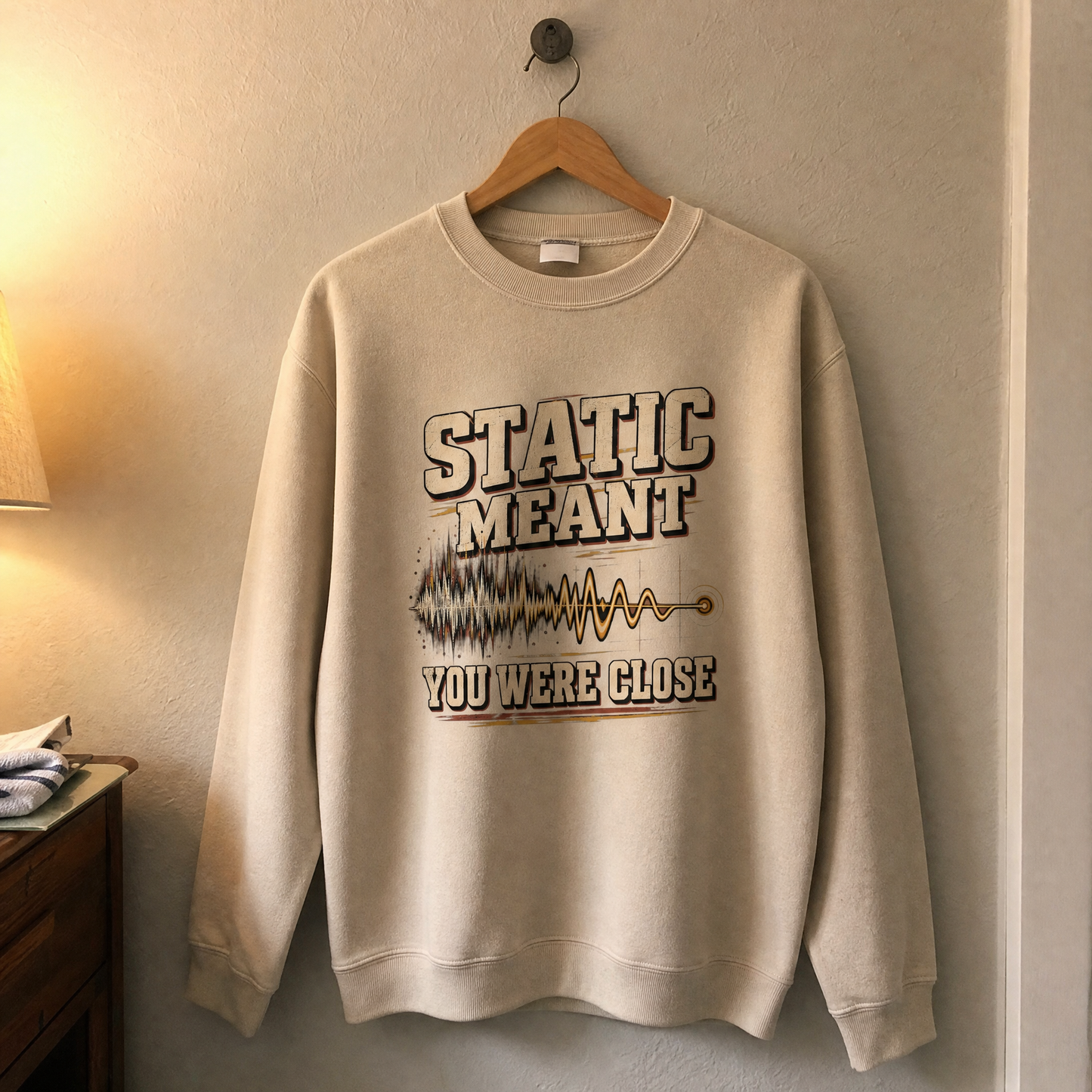 Beige vintage sweatshirt with printed Static Meant You Were Close design, hanging front view indoors.