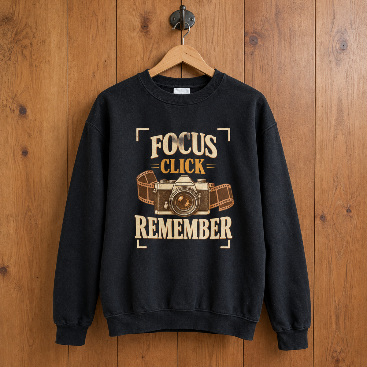 Black vintage sweatshirt with printed Focus Click Remember slogan and camera design, hanging on wooden wall
