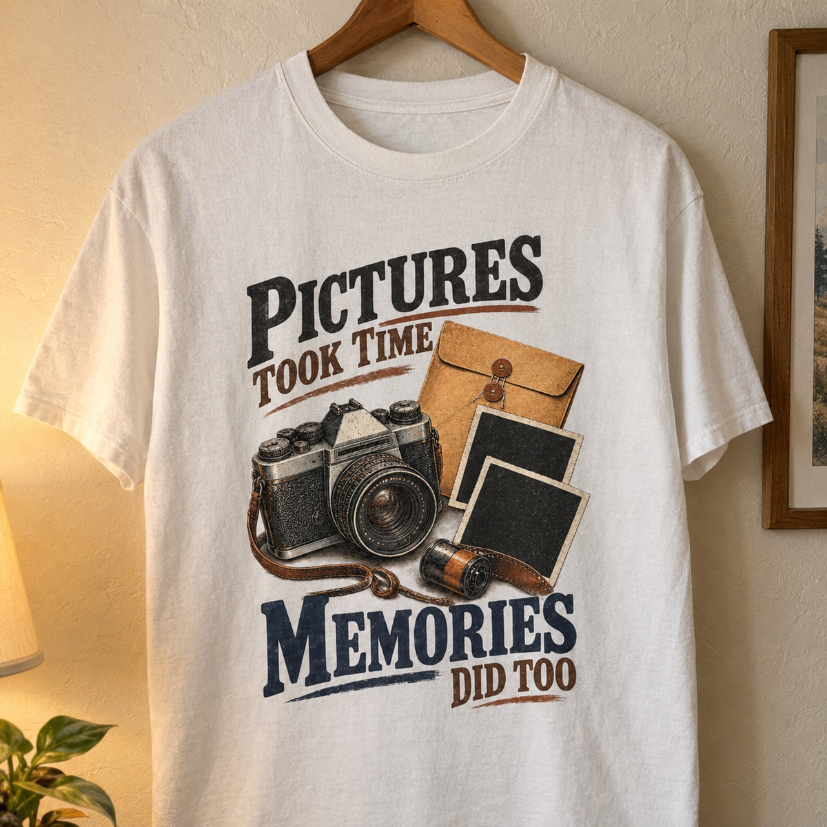 White vintage t-shirt hanging with printed “Pictures Took Time. Memories Did Too” camera design.