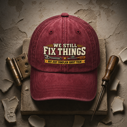 Burgundy vintage washed cap with printed “We Still Fix Things” slogan, front view