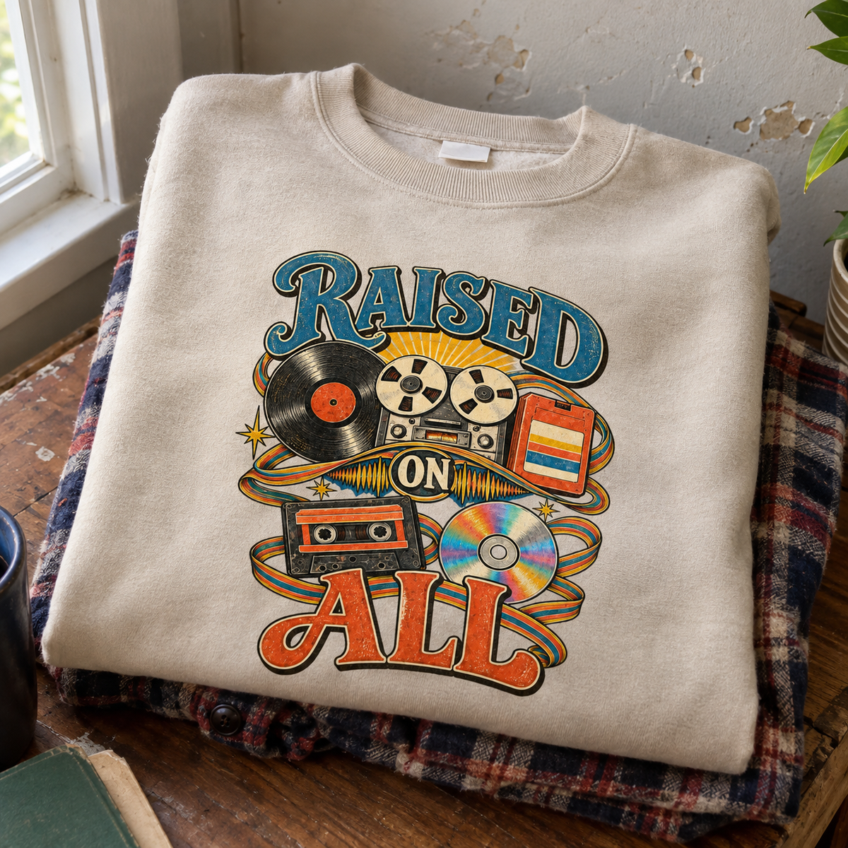 Cream vintage sweatshirt with printed Raised On All retro music graphic, folded on table.