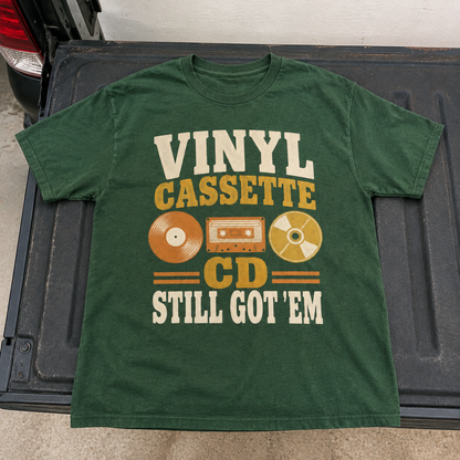 Green vintage t-shirt with printed Vinyl Cassette CD Still Got 'Em design, flat lay hero view