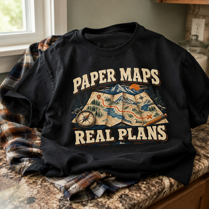 Black vintage t-shirt printed with Paper Maps Real Plans design on rustic indoor setting