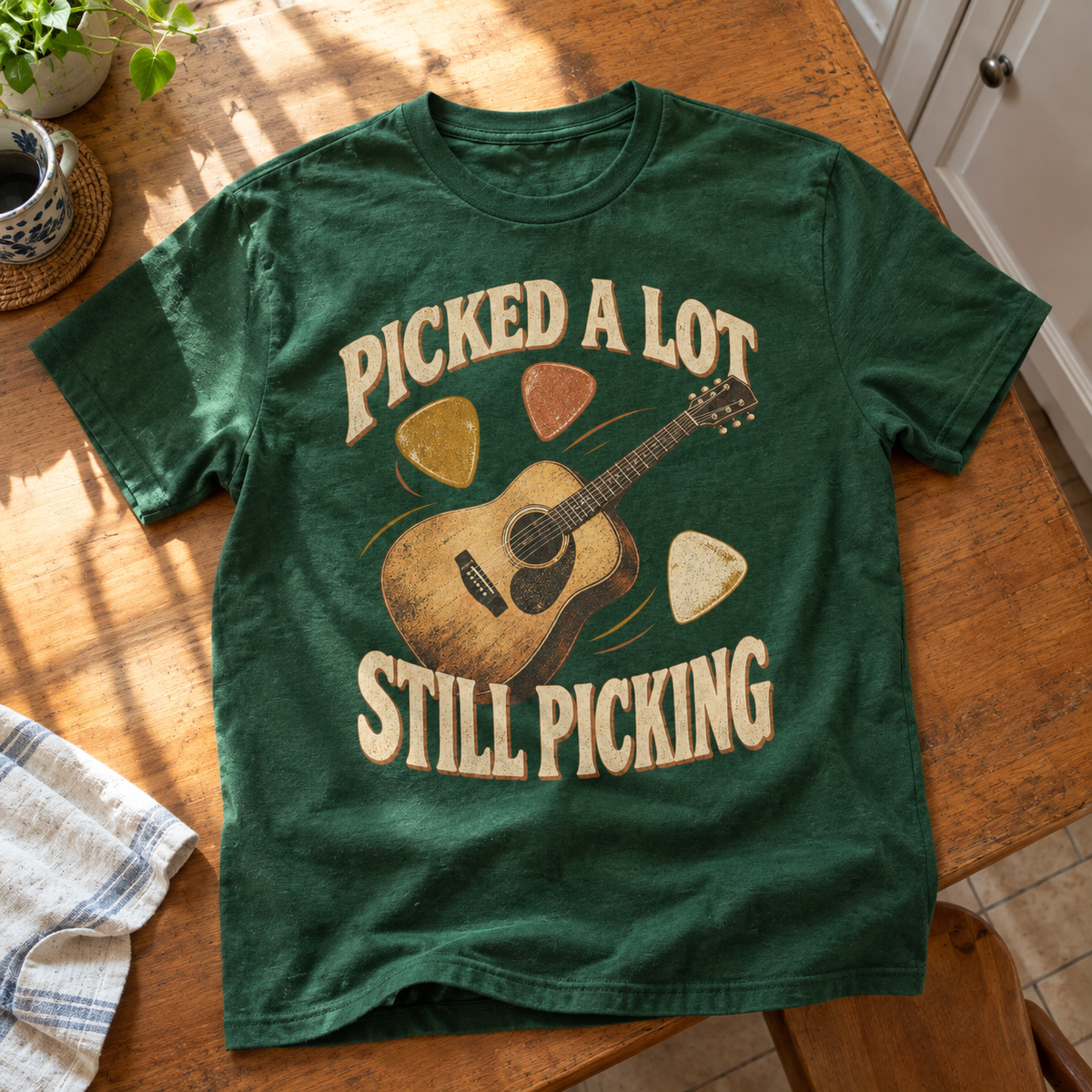Green vintage T-shirt with printed “Picked A Lot Still Picking” guitar design, shown from above.
