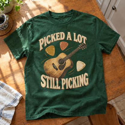 Green vintage T-shirt with printed “Picked A Lot Still Picking” guitar design, shown from above.