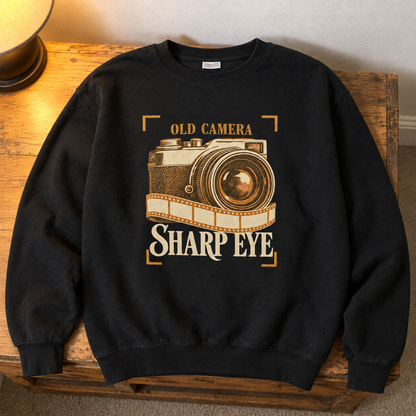 Black vintage sweatshirt with printed Old Camera Sharp Eye design, overhead hero view.