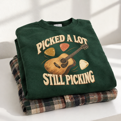 Green vintage sweatshirt printed with “Picked A Lot Still Picking” and guitar design, folded on plaid shirt