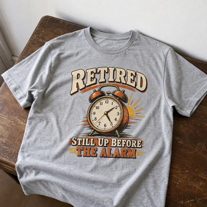 Gray vintage t-shirt featuring printed retired alarm clock slogan, displayed flat on wooden table.